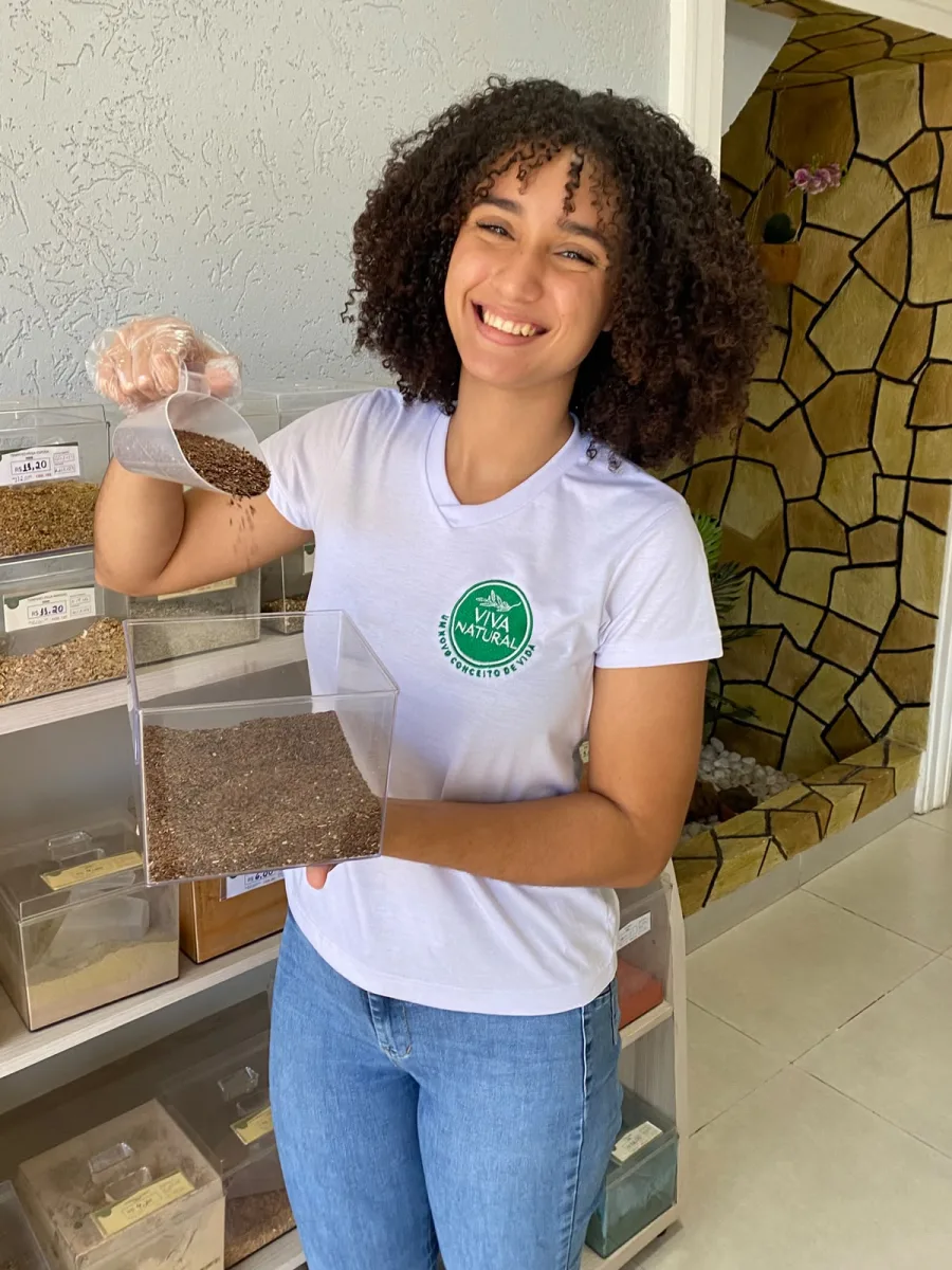 Atendente da Viva Natural servindo sementes com uma concha na área dos granéis